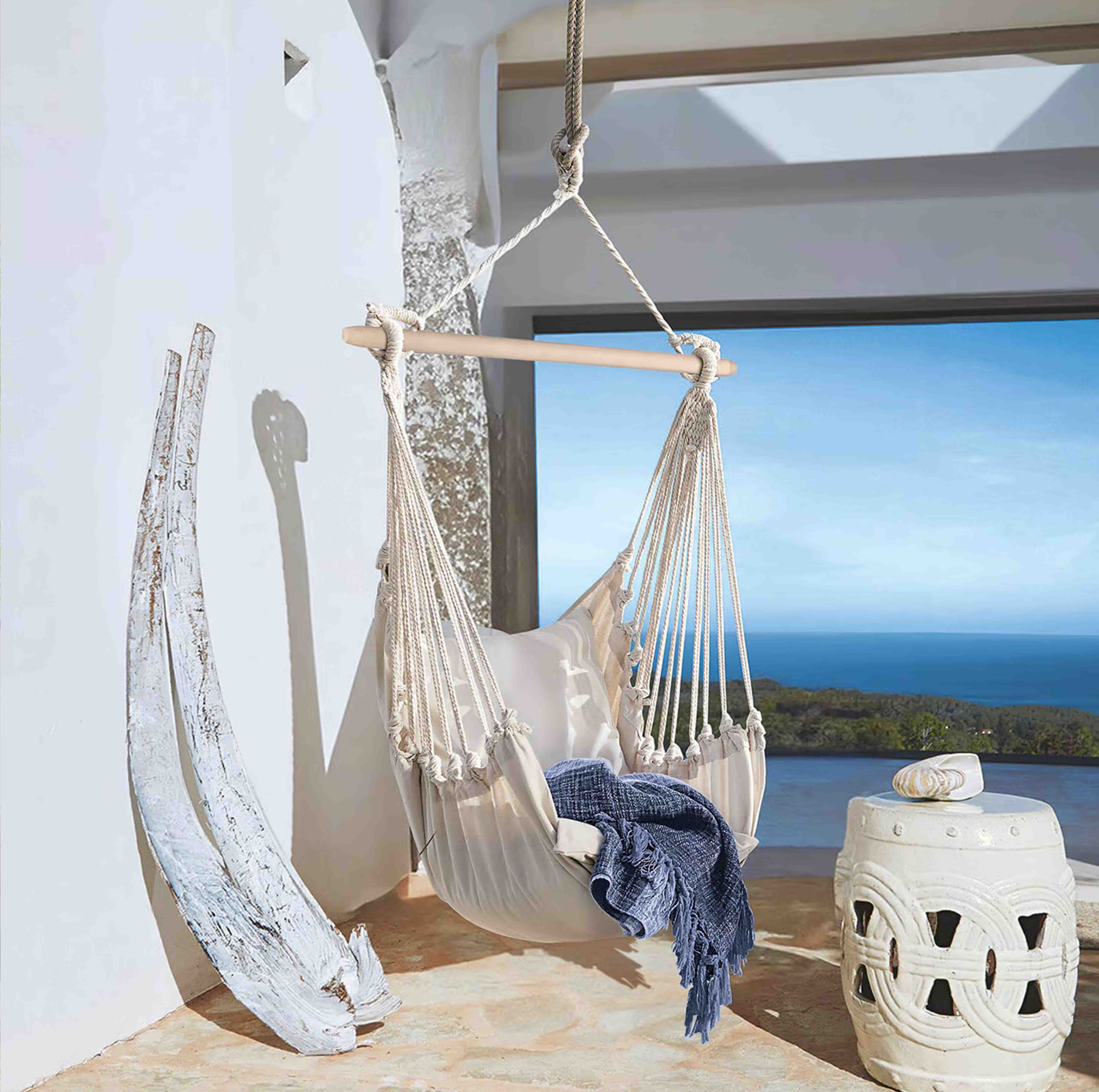 Hamac beige en coton avec barre en bois et couverture bleue sur terrasse avec vue sur la mer