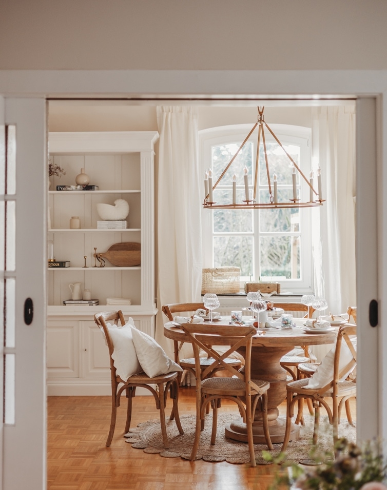 Salle à manger avec table ronde en bois et chaises naturelles sous un lustre à bougies suspendu