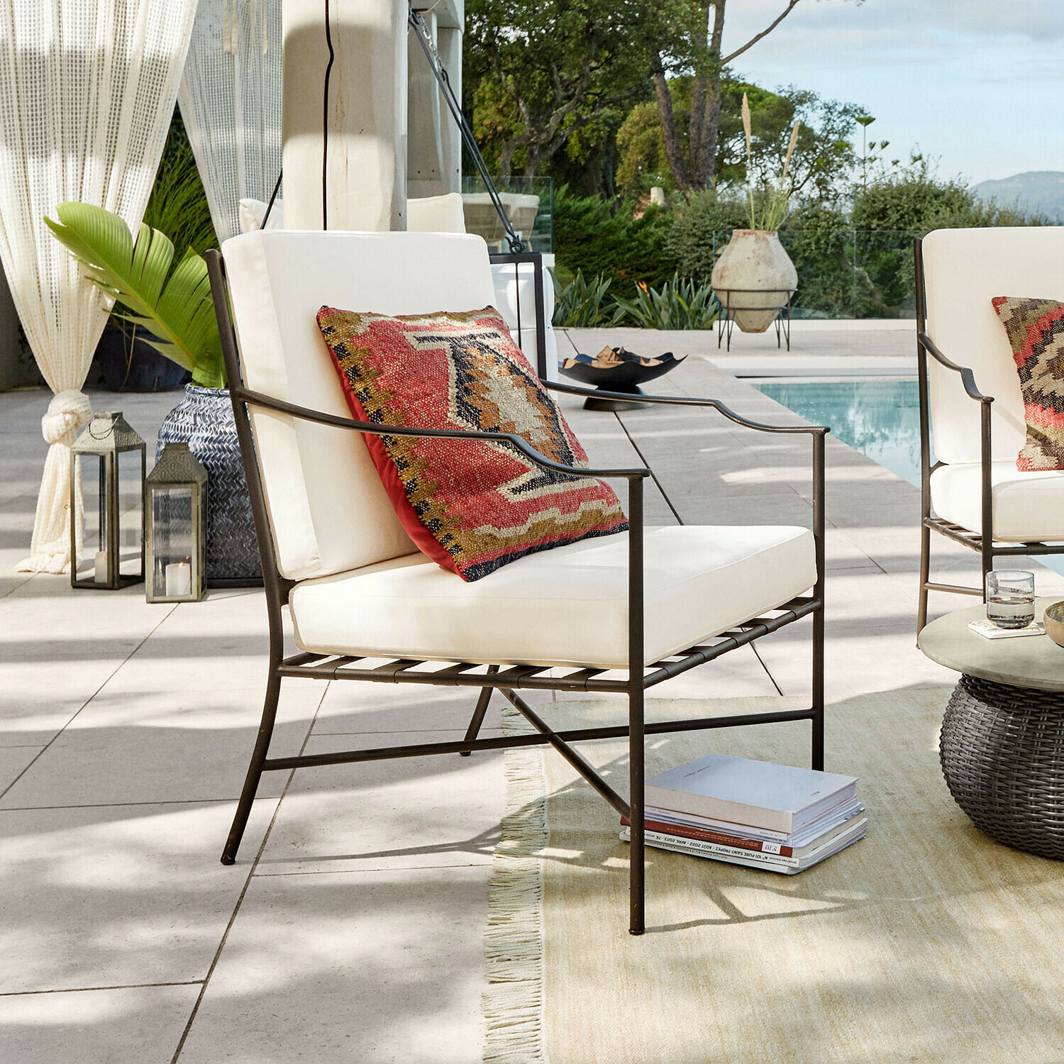 Fauteuil de jardin en métal avec coussins crème et coussin décoratif coloré près de la piscine
