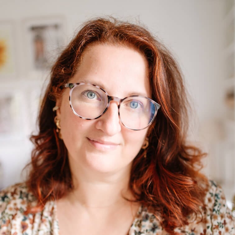 Portrait d'une femme aux cheveux roux et lunettes dans un intérieur lumineux flou