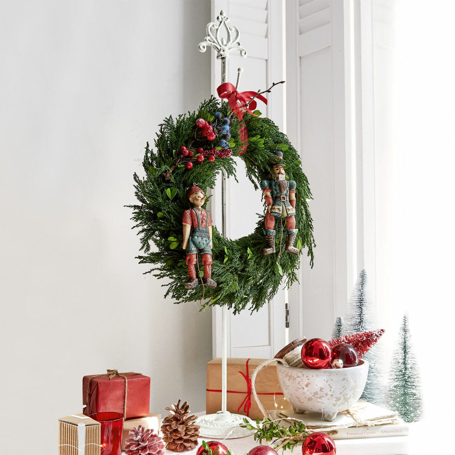 Support pour couronne Irulan Couronne de Noël en branches vertes avec baies rouges et bleues et figurines en bois sur support blanc