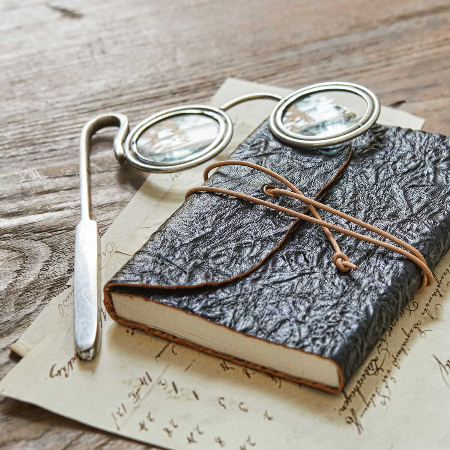 Loupe Robert Carnet noir en cuir souple avec lien en corde sur table en bois avec lunettes et lettres anciennes