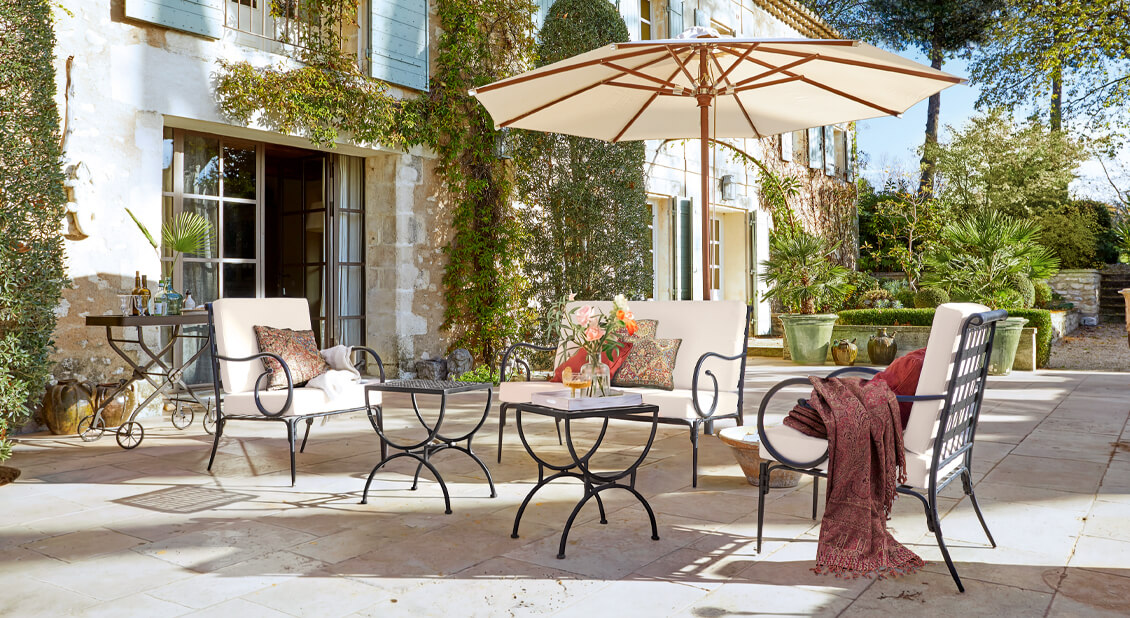 Ensemble de mobilier de jardin en métal avec coussins crème sous un parasol sur une terrasse en pierre