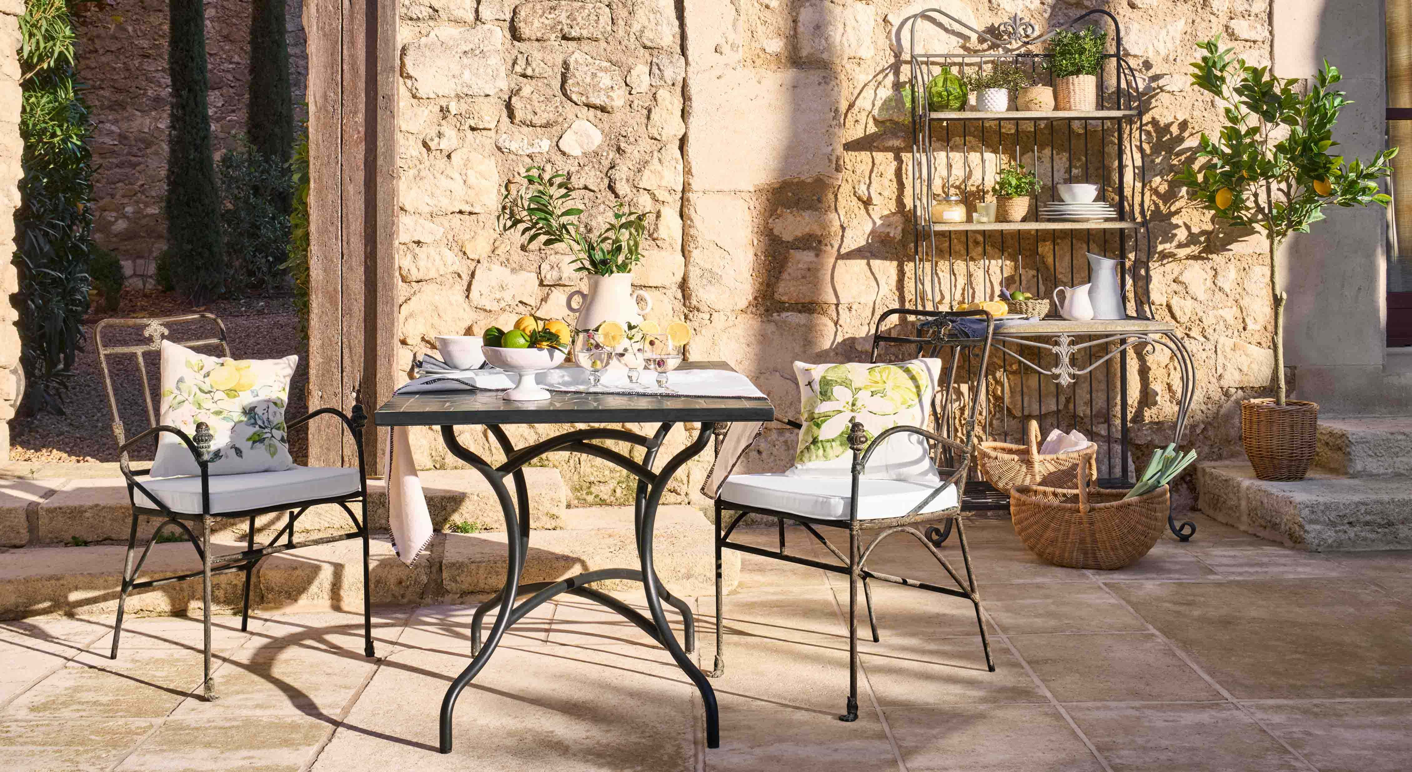 Table et chaises en métal avec coussins à motifs floraux sur patio en pierre avec décorations de jardin