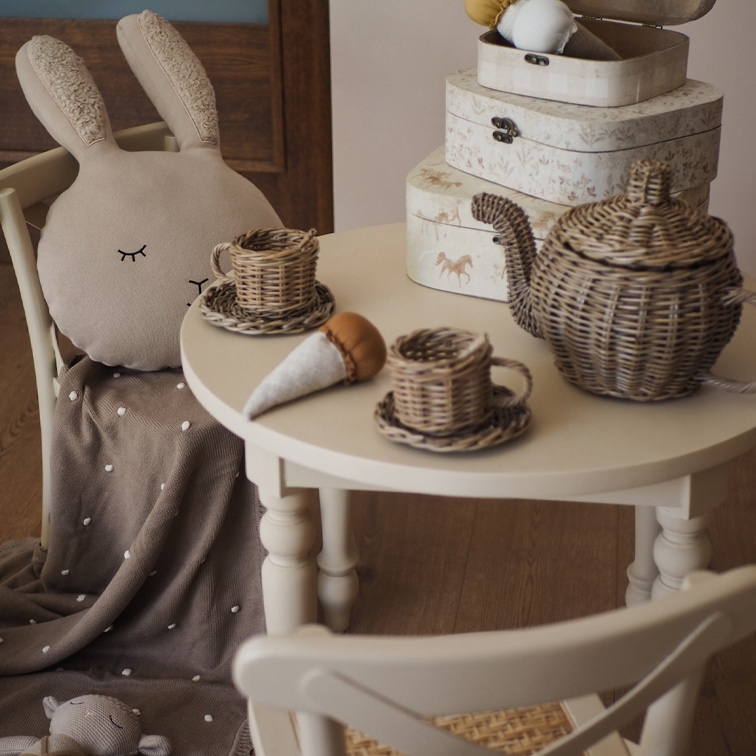 Service à thé en osier sur table blanche avec coussin lapin en peluche et couverture marron