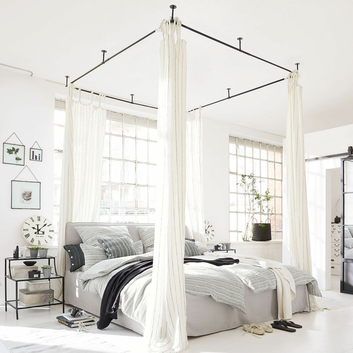 Ciel de lit Giroux Lit à baldaquin moderne en tissu gris clair avec rideaux blancs dans une chambre lumineuse aux grandes fenêtres