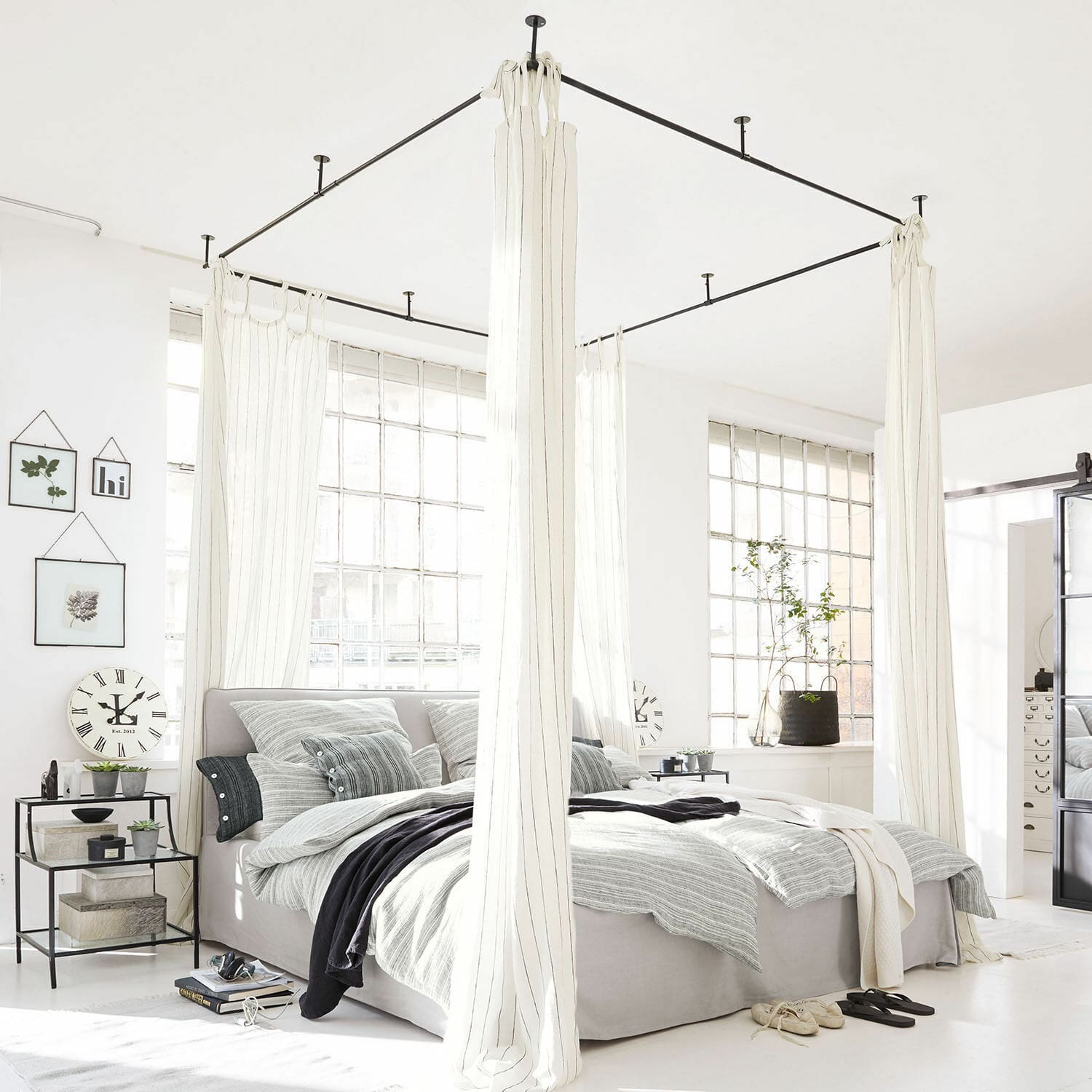 Ciel de lit Giroux Lit à baldaquin moderne en tissu gris clair avec rideaux blancs dans une chambre lumineuse aux grandes fenêtres