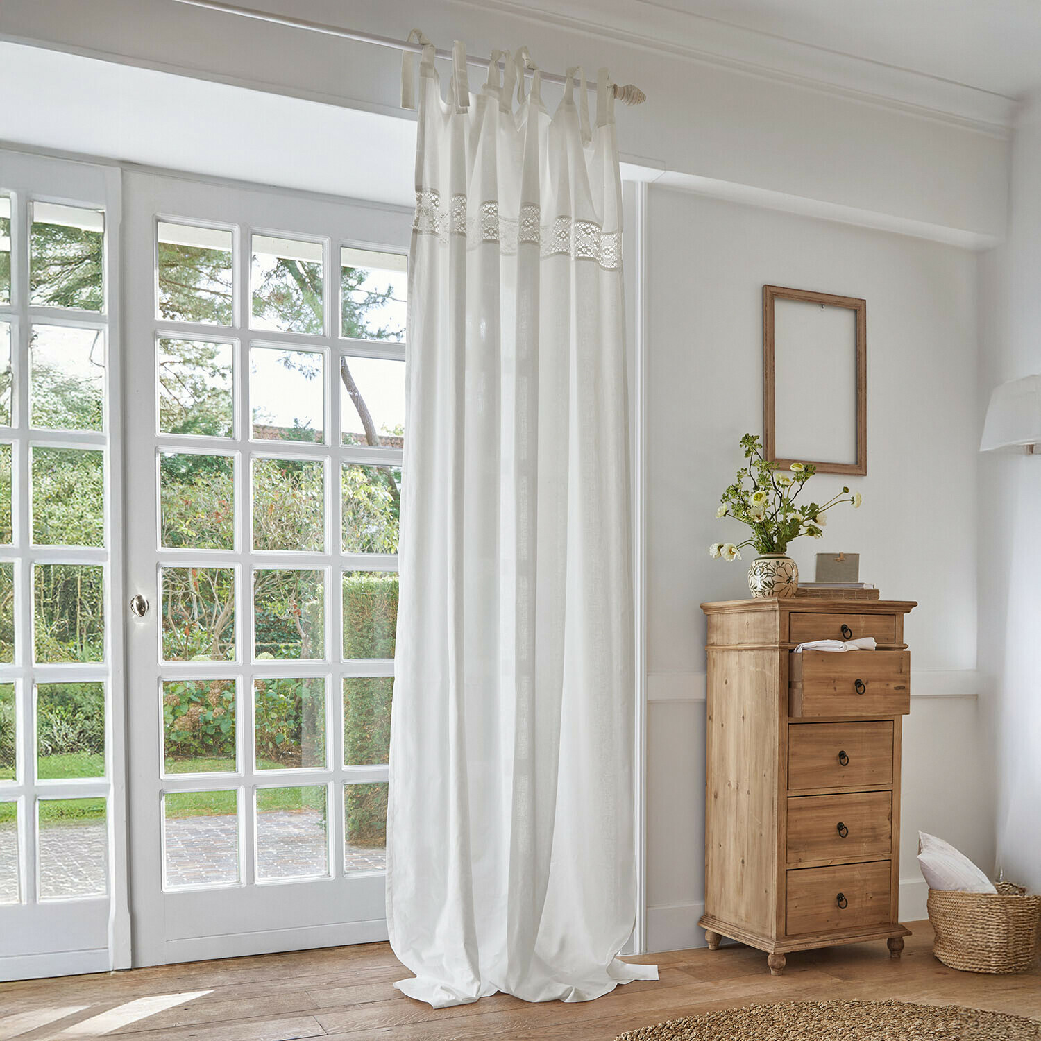 Voilage Isolineas Rideau blanc en coton avec bande en dentelle dans une pièce lumineuse avec commode en bois naturel