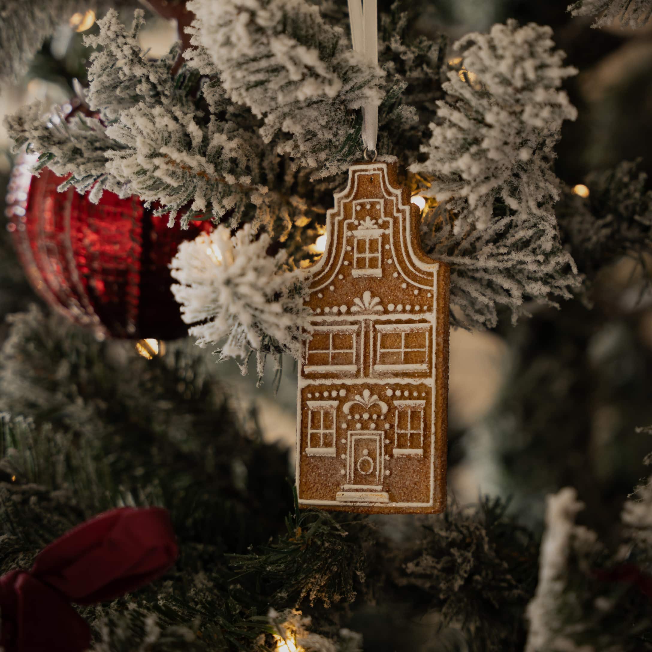 Décoration de sapin en forme de maison en pain d'épice avec motifs blancs sur branches vertes enneigées artificiellement