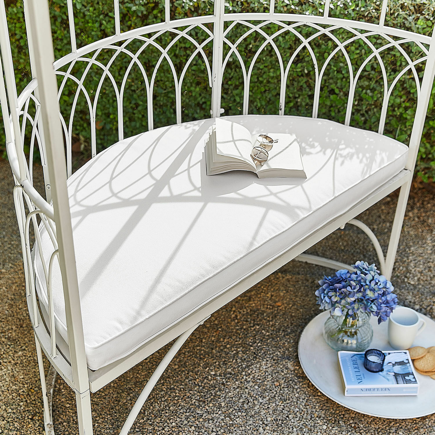 Coussin d’assise Drivesto Banc de jardin en métal blanc avec coussin blanc, livre ouvert, fleurs bleues et tasse sur terrasse