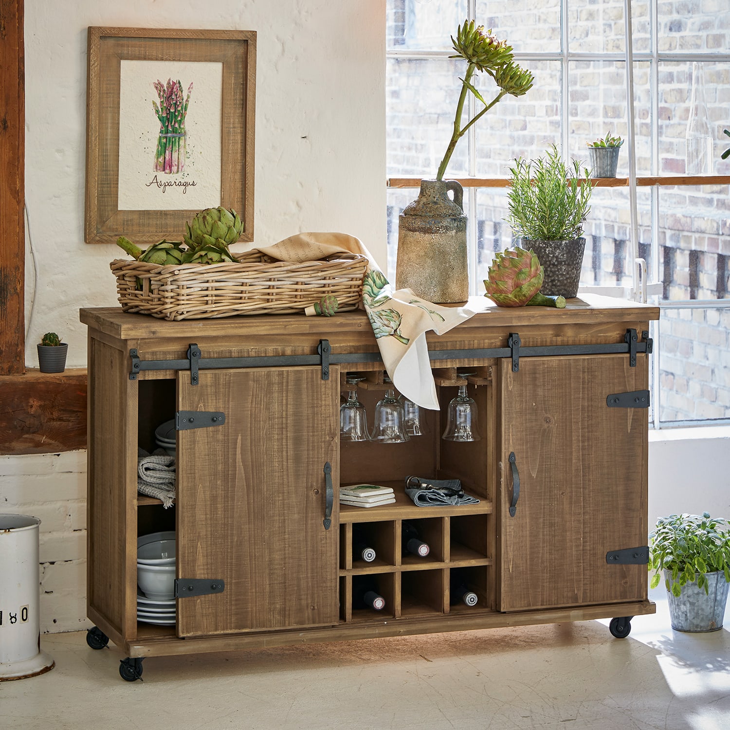 Buffet en bois sur roulettes avec rangement à vin et verres, décoré de plantes et panier de légumes