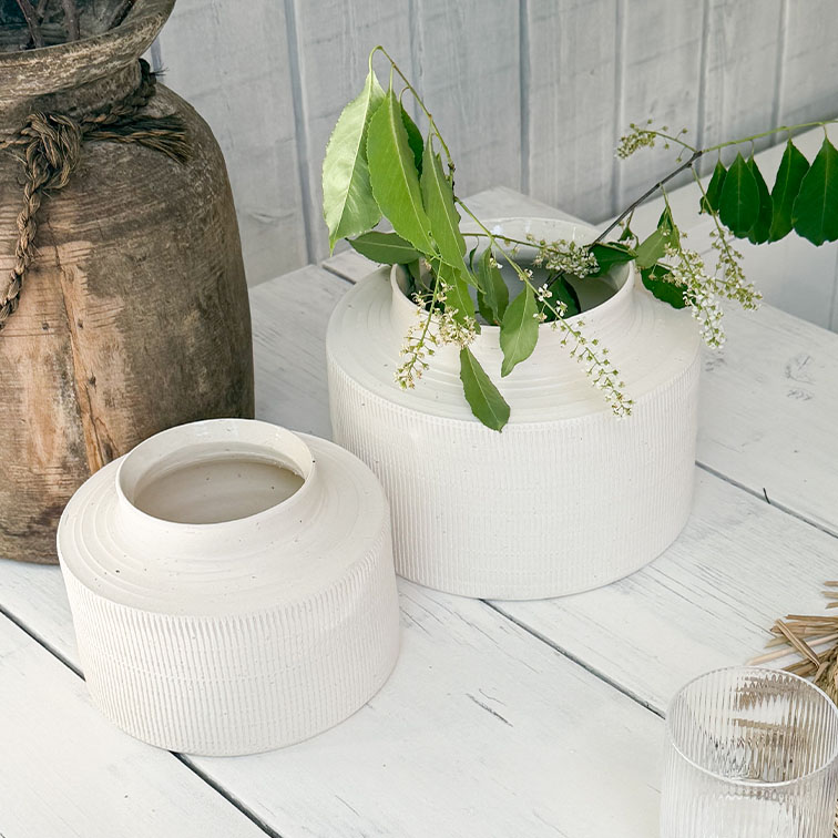 Vases en céramique blanche mate sur table en bois avec feuillage vert et petites fleurs blanches