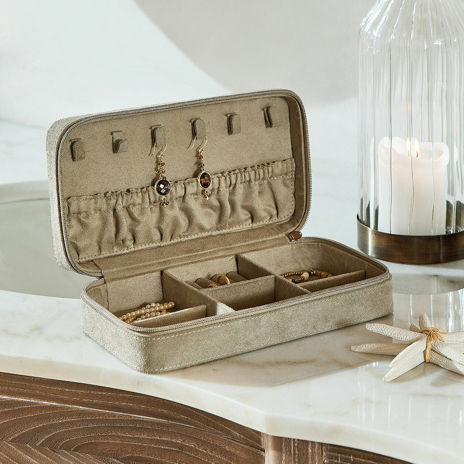 Coffret à bijoux Angelique Écrin à bijoux en daim beige avec compartiments et crochets pour boucles d'oreilles sur un comptoir en marbre