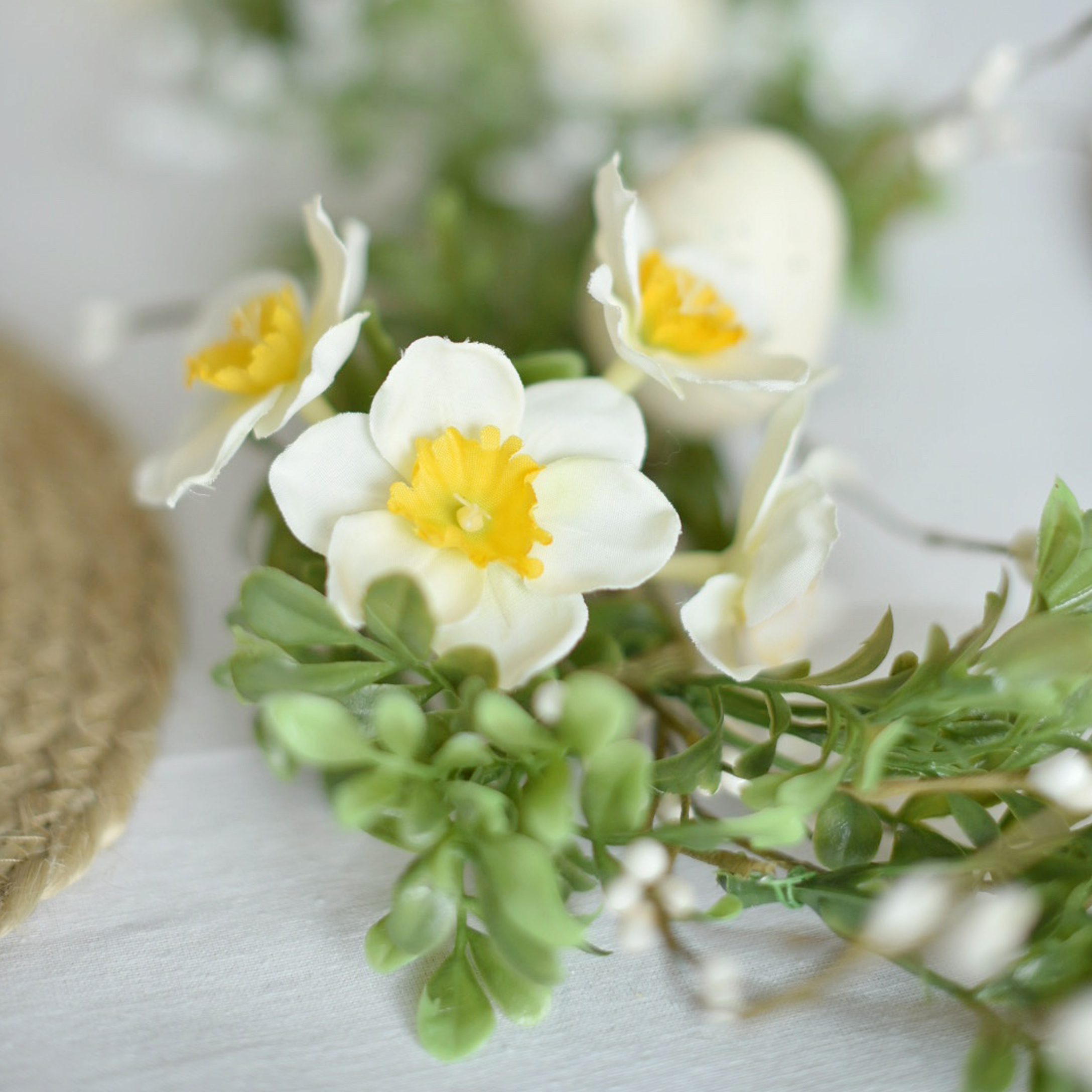 Couronne décorative avec fleurs blanches et jaunes et feuillage vert sur fond clair
