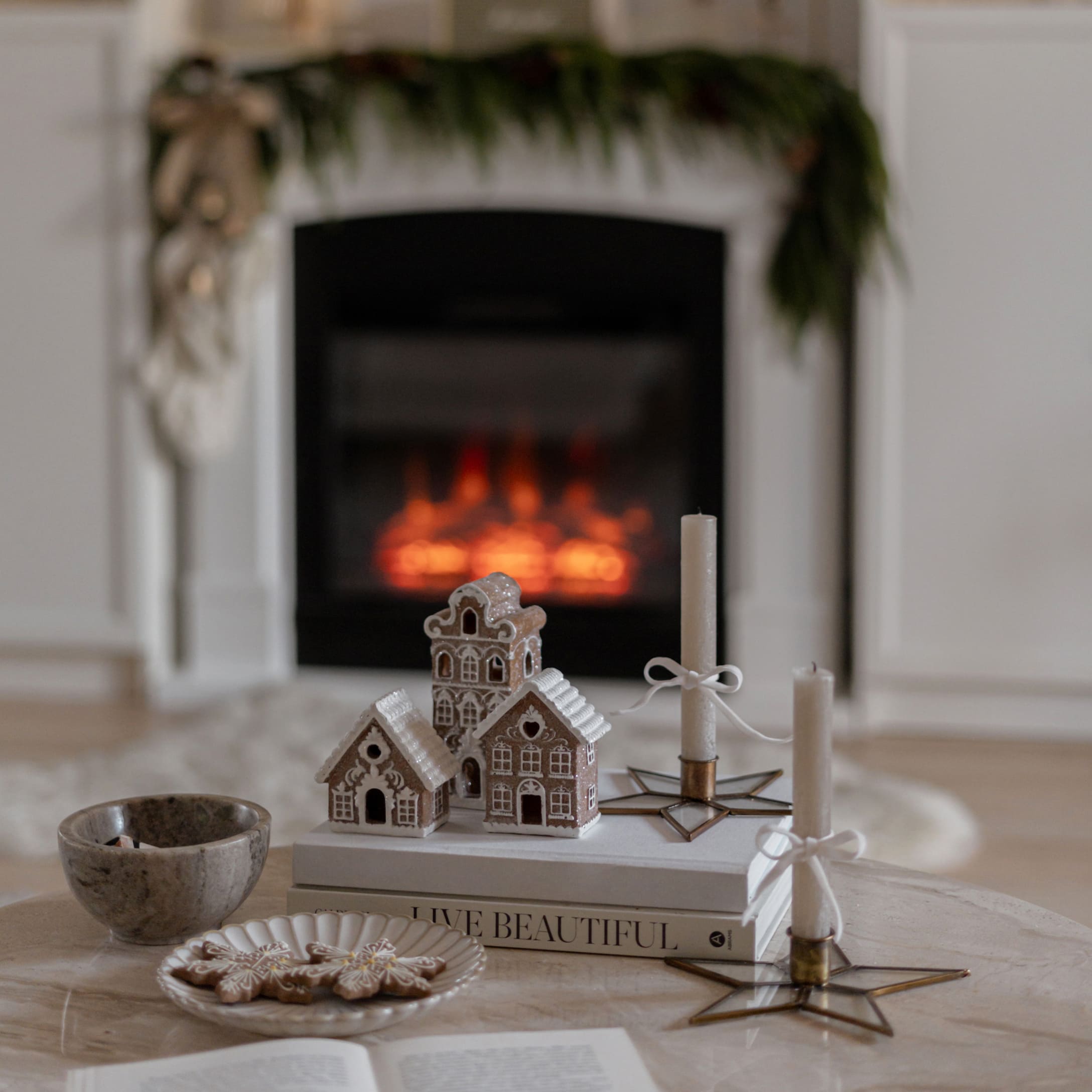 Maisons en pain d'épice décoratives et bougies blanches sur des livres devant une cheminée festive
