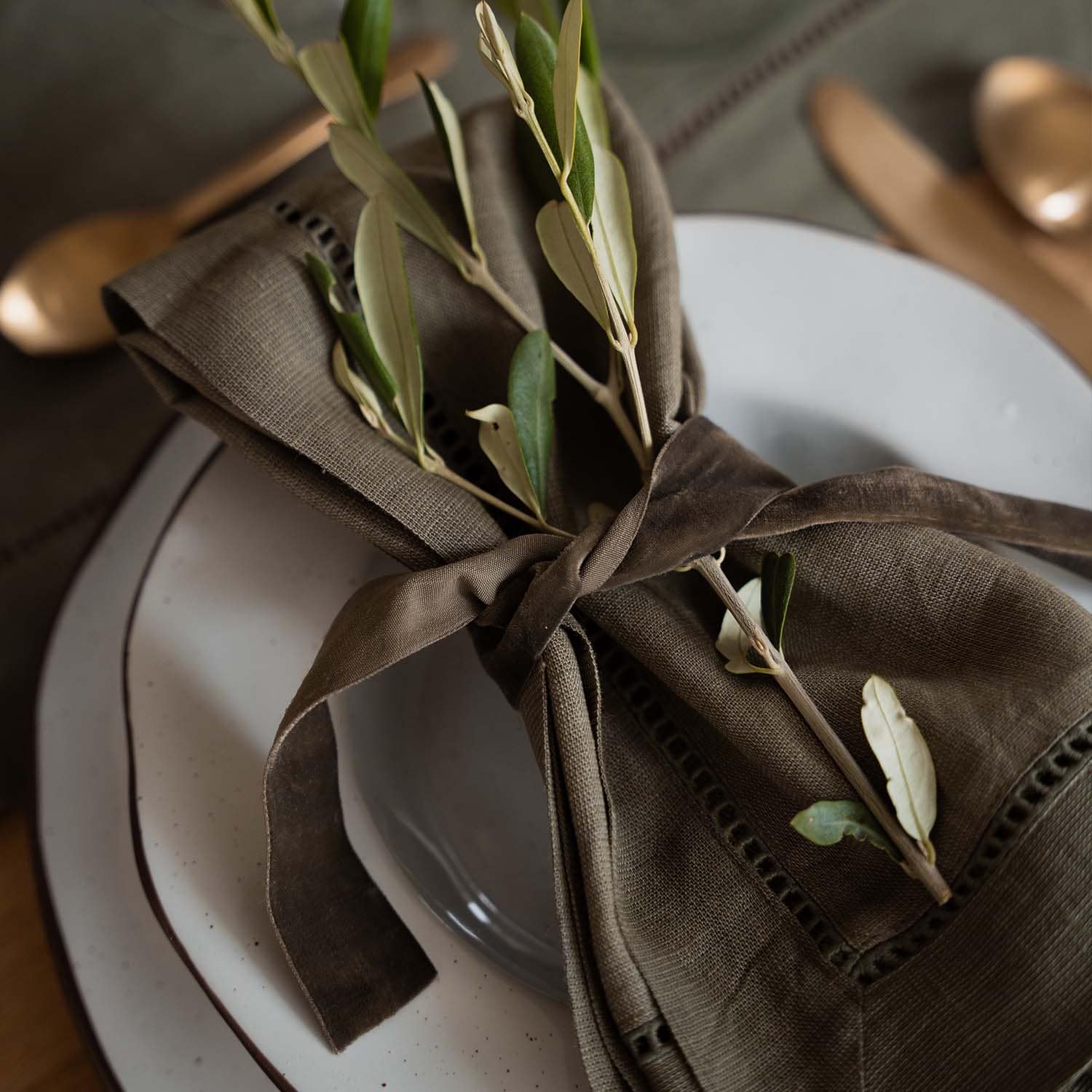 Serviette en lin marron avec branches vertes sur assiette blanche, décoration de table élégante