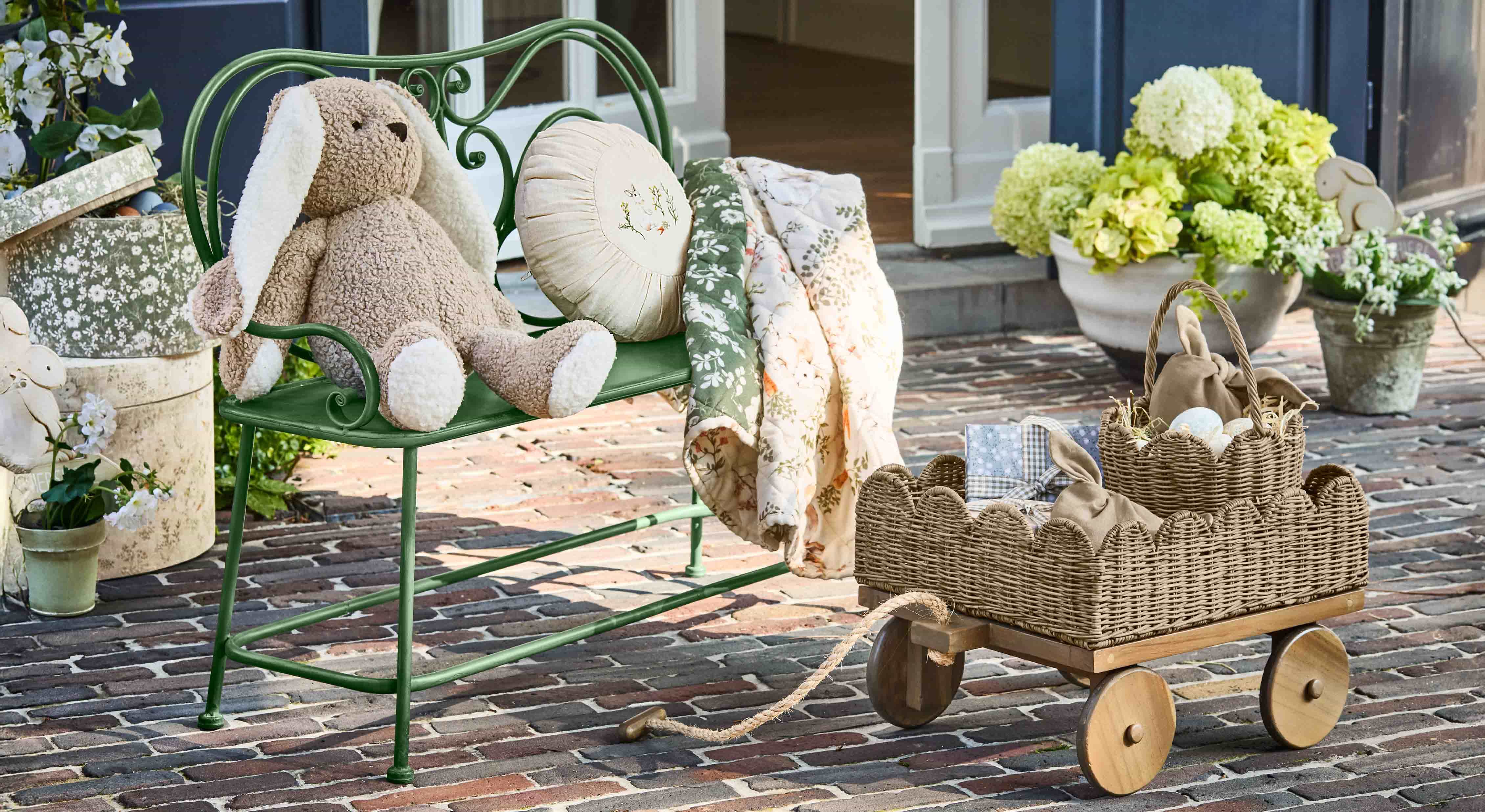 Banc vert en métal avec peluche lapin beige et couverture fleurie sur patio pavé