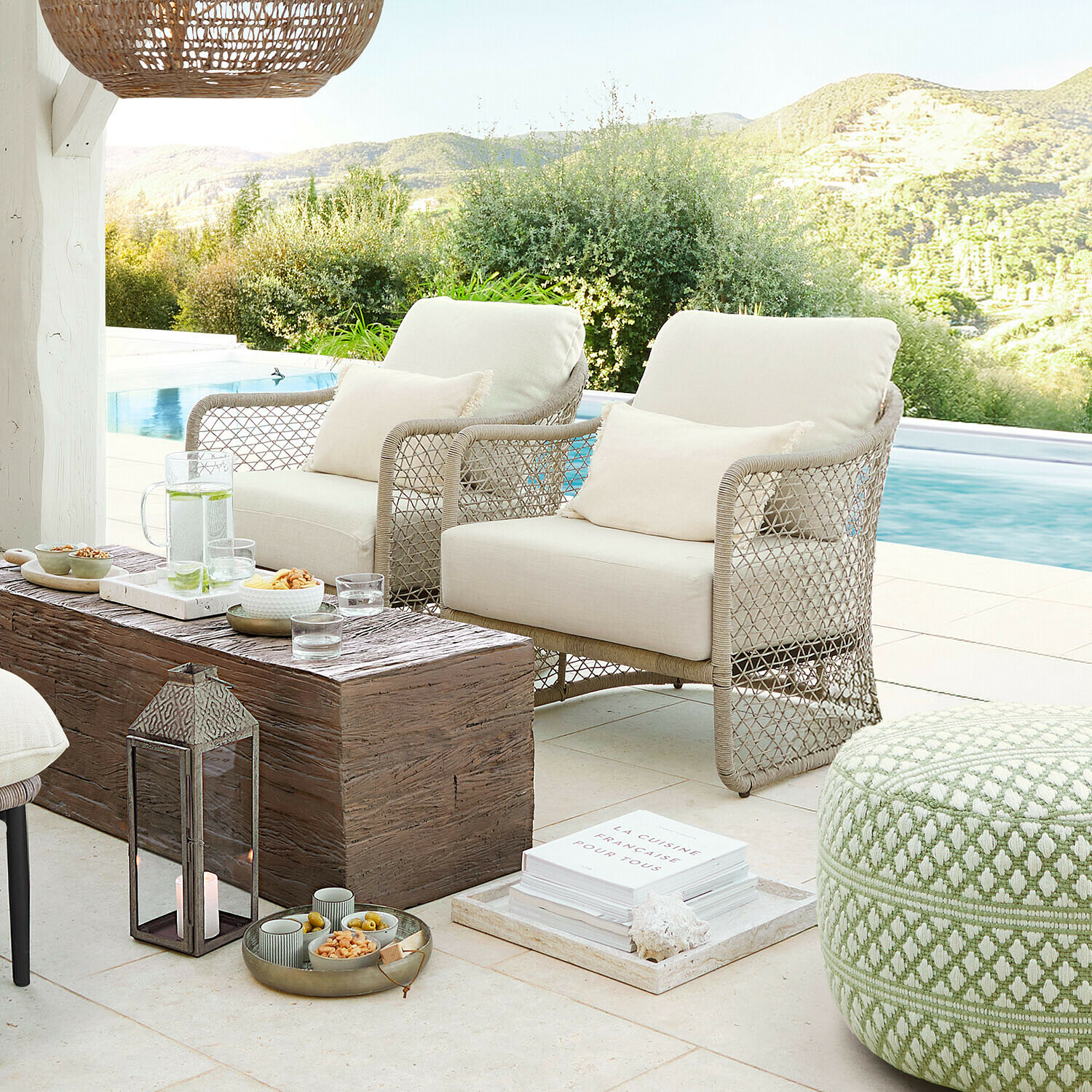 Deux fauteuils beige en matériau tressé sur terrasse près de la piscine avec table en bois et pouf vert
