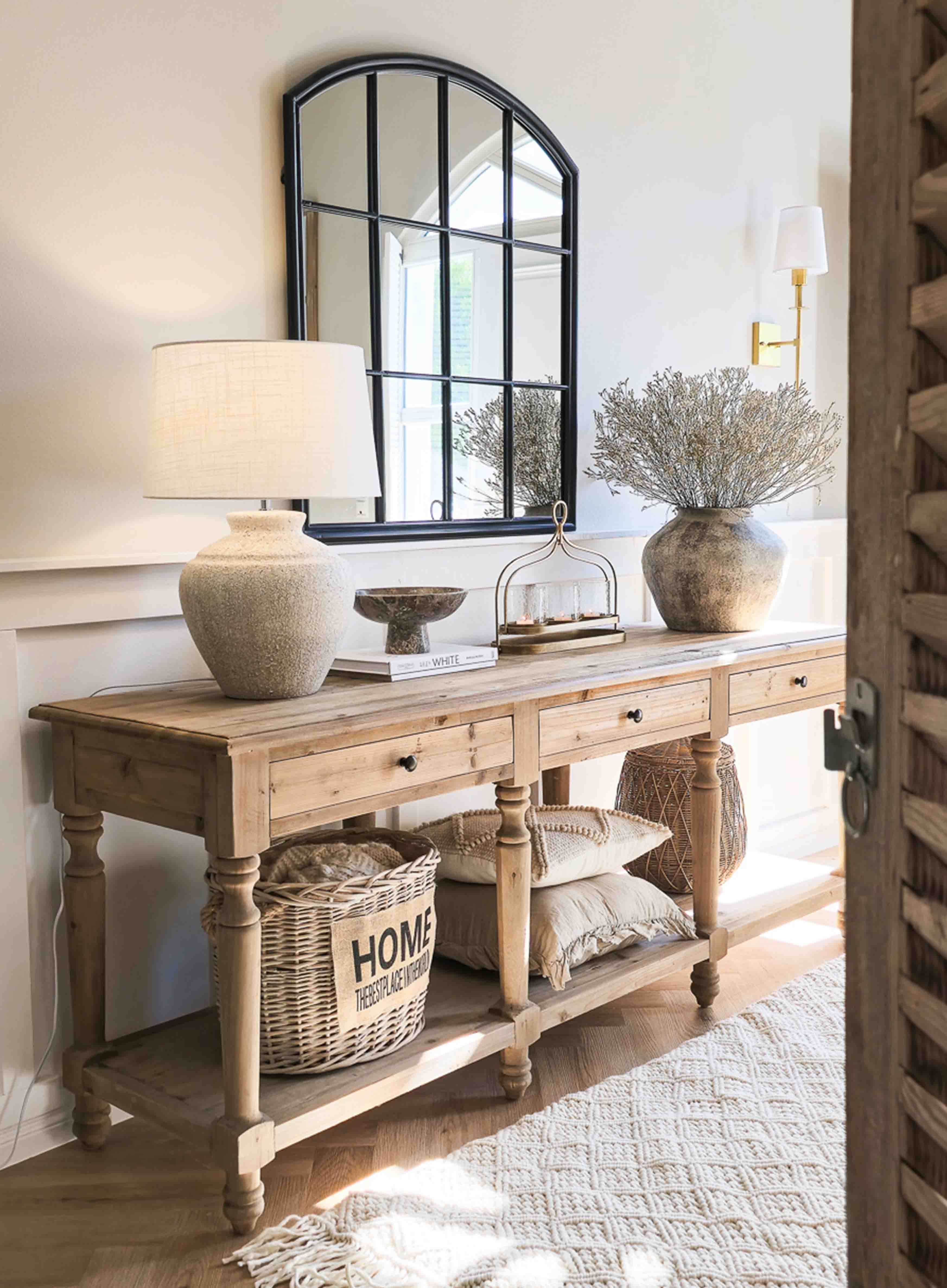 Console en bois avec lampe en céramique, miroir à cadre noir et décoration rustique dans un intérieur lumineux