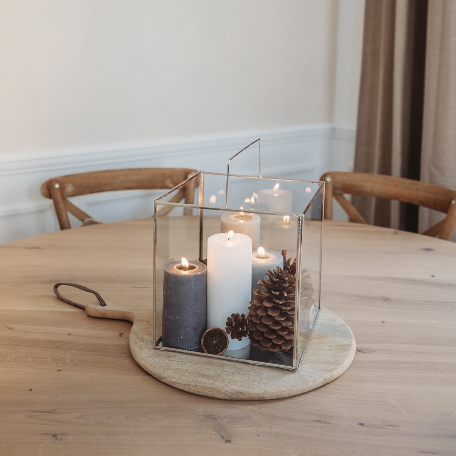 Lanterne en verre avec trois bougies et pommes de pin sur planche en bois, décoration de Noël