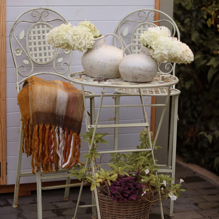 Table et deux chaises en métal vintage couleur claire avec vases décoratifs et fleurs blanches