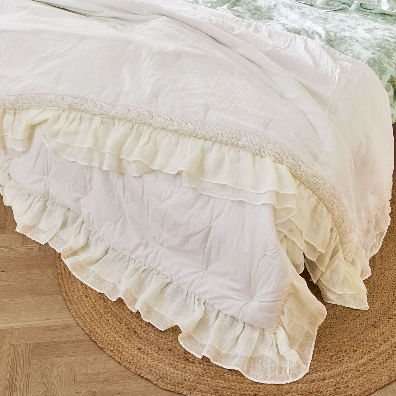 Courtepointe Jolévianne Couvre-lit blanc avec volants et bordure en dentelle posé sur un tapis en jute