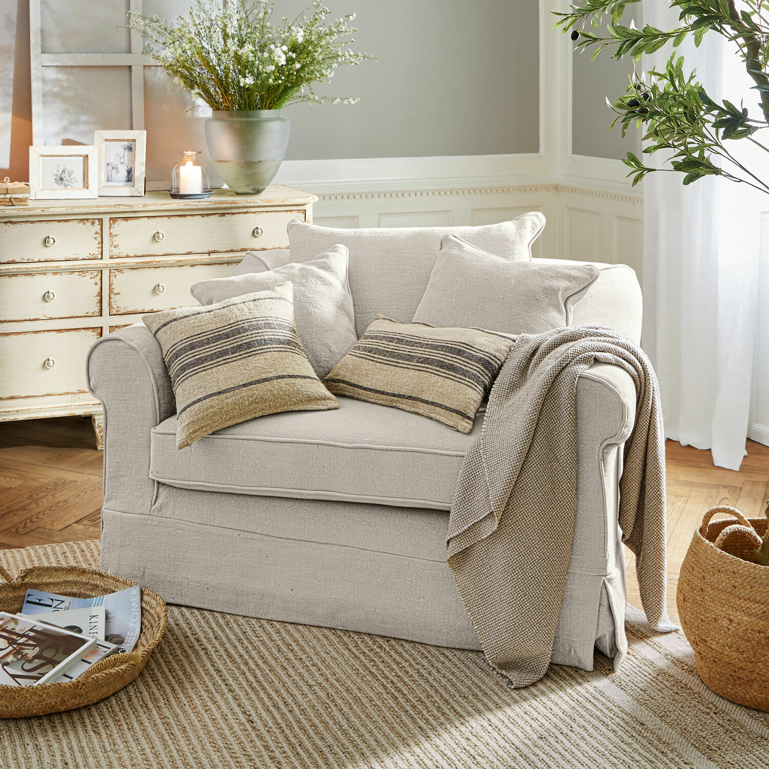 Fauteuil Folsom Canapé beige en tissu avec coussins rayés et plaid dans un salon chaleureux avec tapis naturel