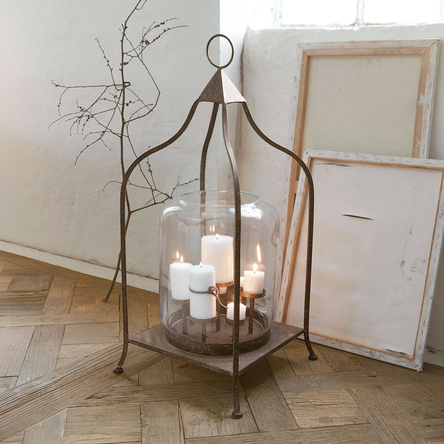 Lanterne en métal avec abat-jour en verre transparent et bougies blanches sur parquet en bois