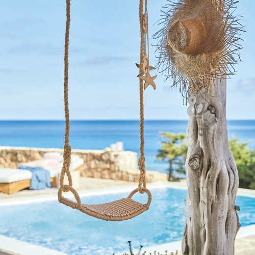 Balançoire en corde tressée devant une piscine avec vue sur la mer, ambiance estivale