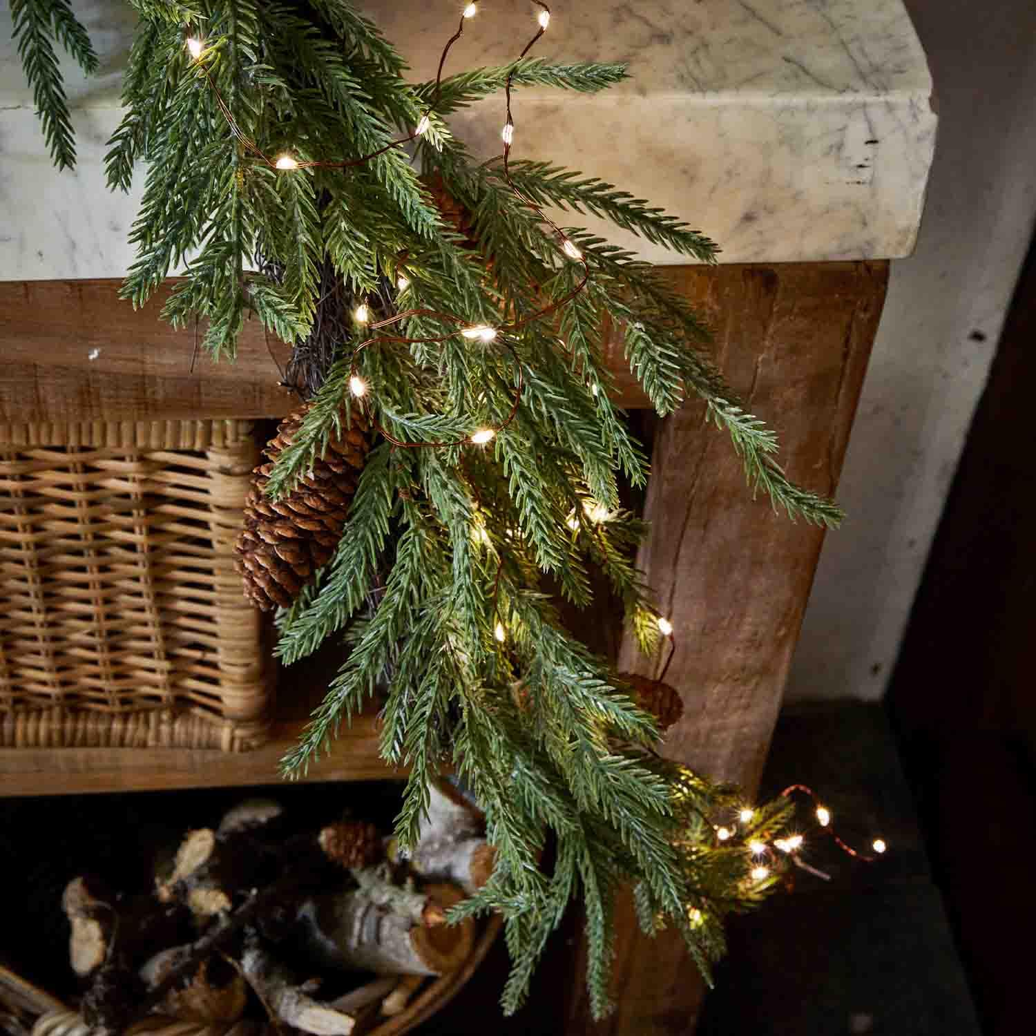 Branche de sapin avec pomme de pin et guirlande lumineuse LED sur cheminée en bois, décoration festive