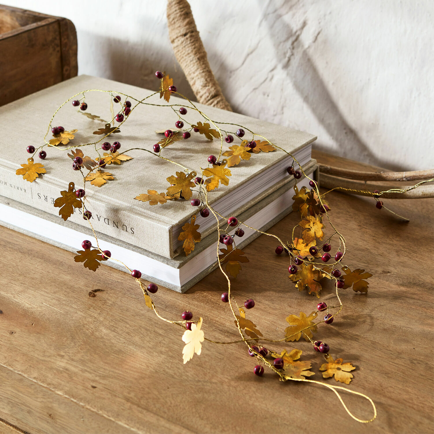 Guirlande Liezel Guirlande décorative en métal doré avec feuilles et baies rouges posée sur une table en bois