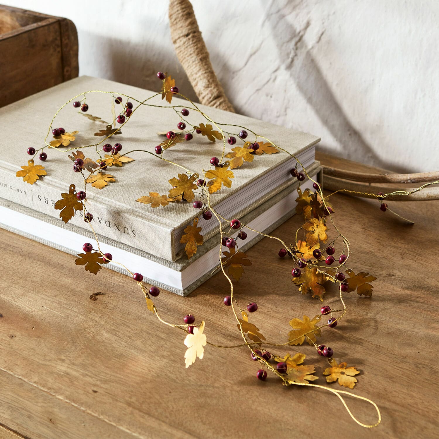 Guirlande Liezel Guirlande décorative en métal doré avec feuilles et baies rouges posée sur une table en bois