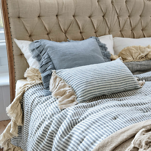 Coussins en lin beige et bleu avec une couverture rayée sur une tête de lit capitonnée beige