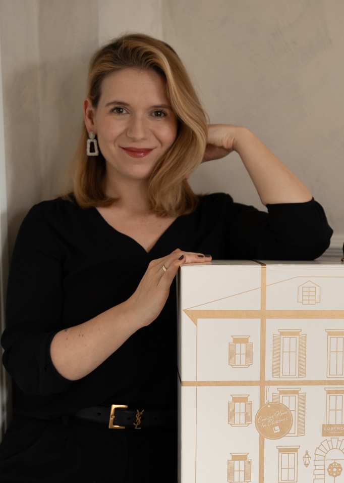 Femme en haut noir appuyée sur une grande boîte blanche avec dessin de maison, thème de Noël