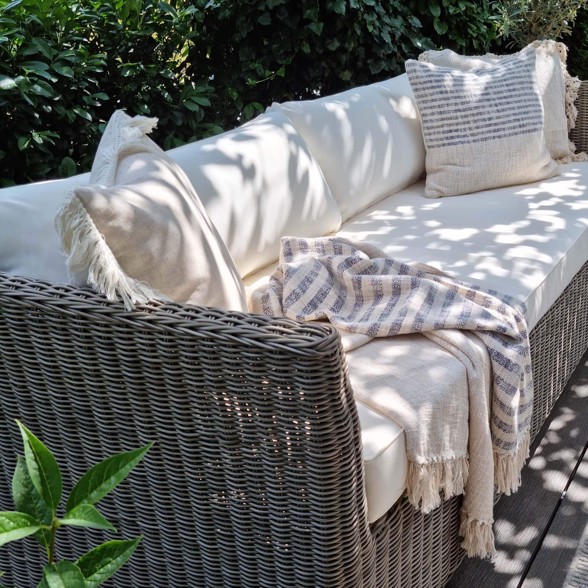Canapé d'extérieur en rotin gris avec coussins crème et plaid beige rayé pour jardin
