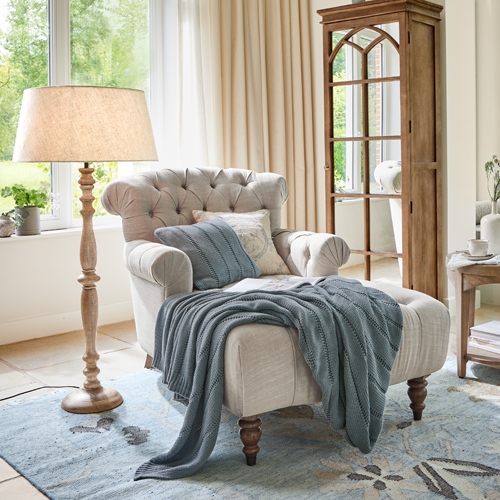 Fauteuil beige capitonné avec pieds en bois et plaid bleu dans un salon lumineux