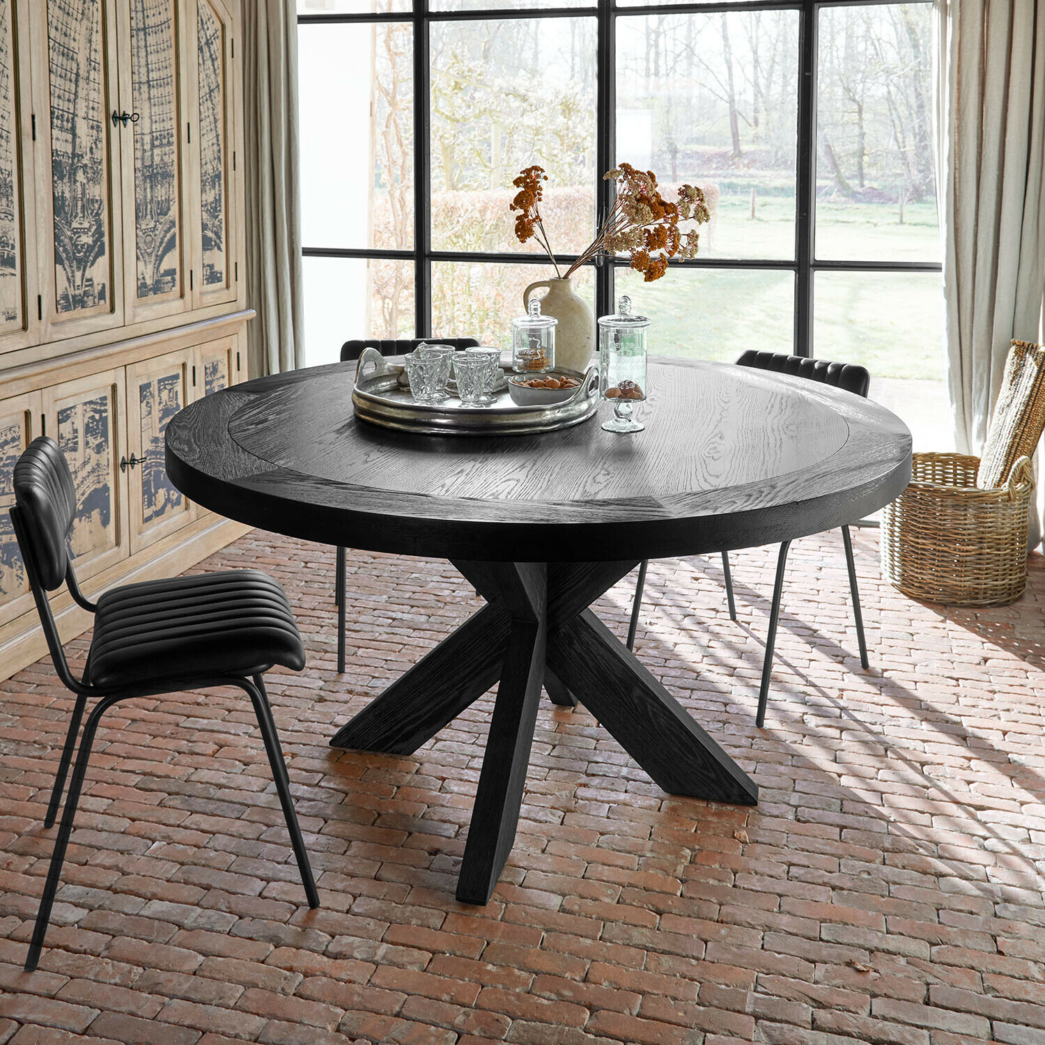 Table Darvoux Table ronde en bois noir avec plateau décoratif et fleurs séchées dans une pièce lumineuse au sol en briques
