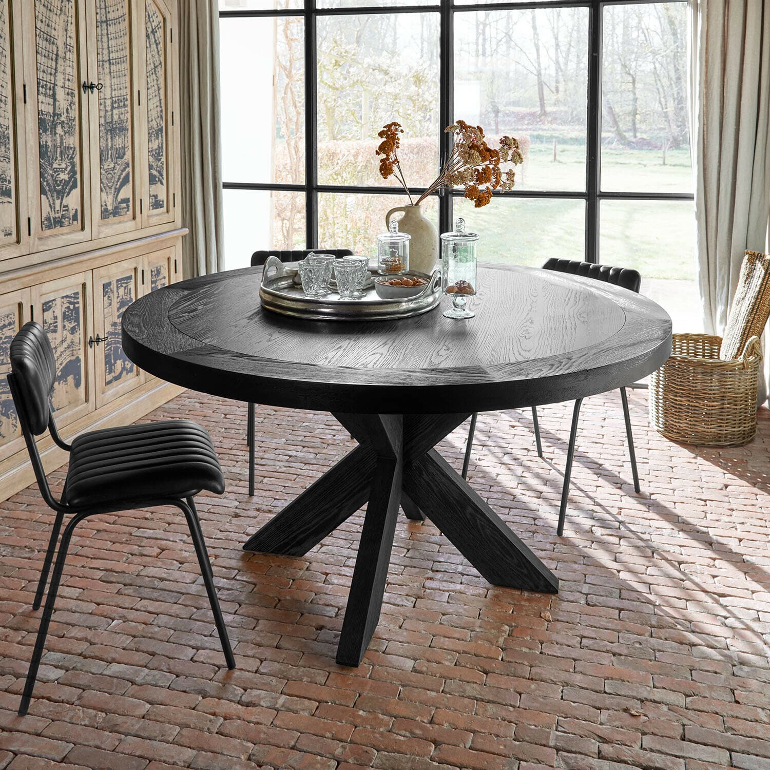 Table Darvoux Table ronde en bois noir avec plateau décoratif et fleurs séchées dans une pièce lumineuse au sol en briques