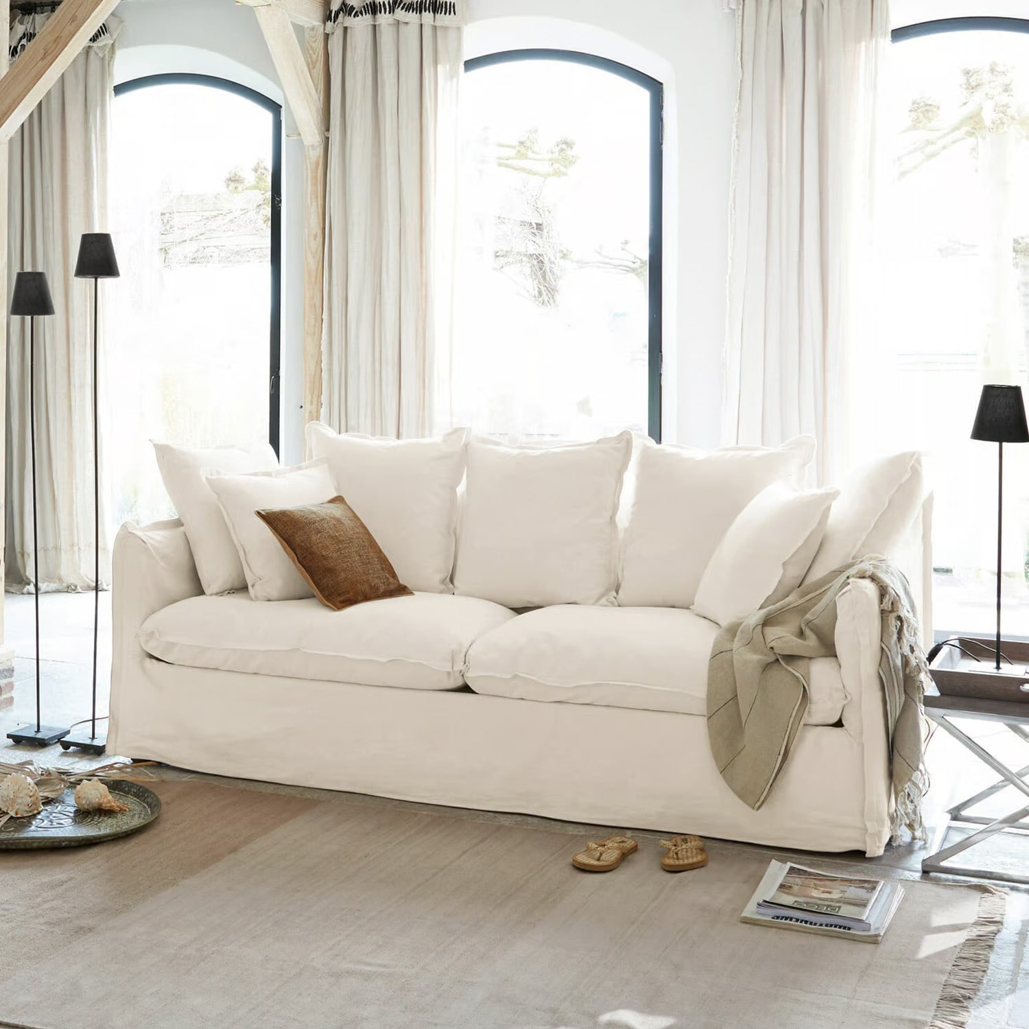Grand canapé blanc en coton avec coussins et coussin décoratif marron dans un salon lumineux