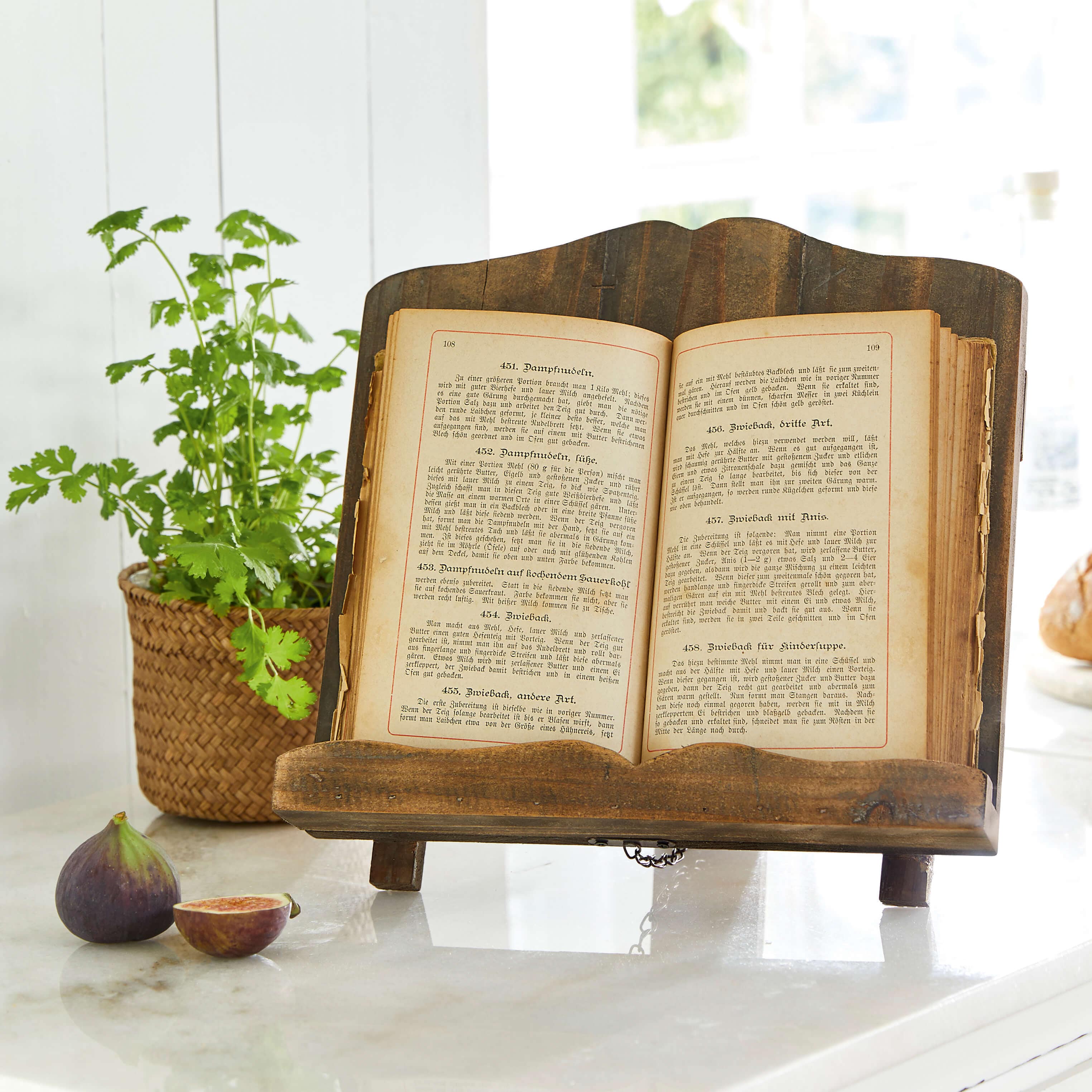 Porte-livre en bois foncé avec un vieux livre de cuisine ouvert sur un plan de travail en marbre