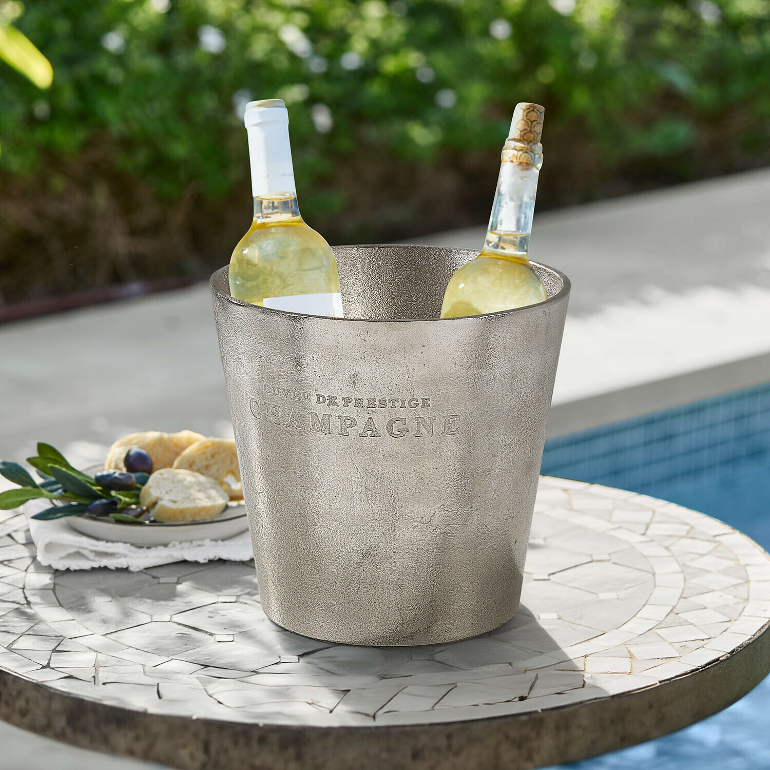 Seau à glace Marclaire Seau à glace en métal argenté avec inscription Champagne contenant deux bouteilles de vin blanc sur une table extérieure