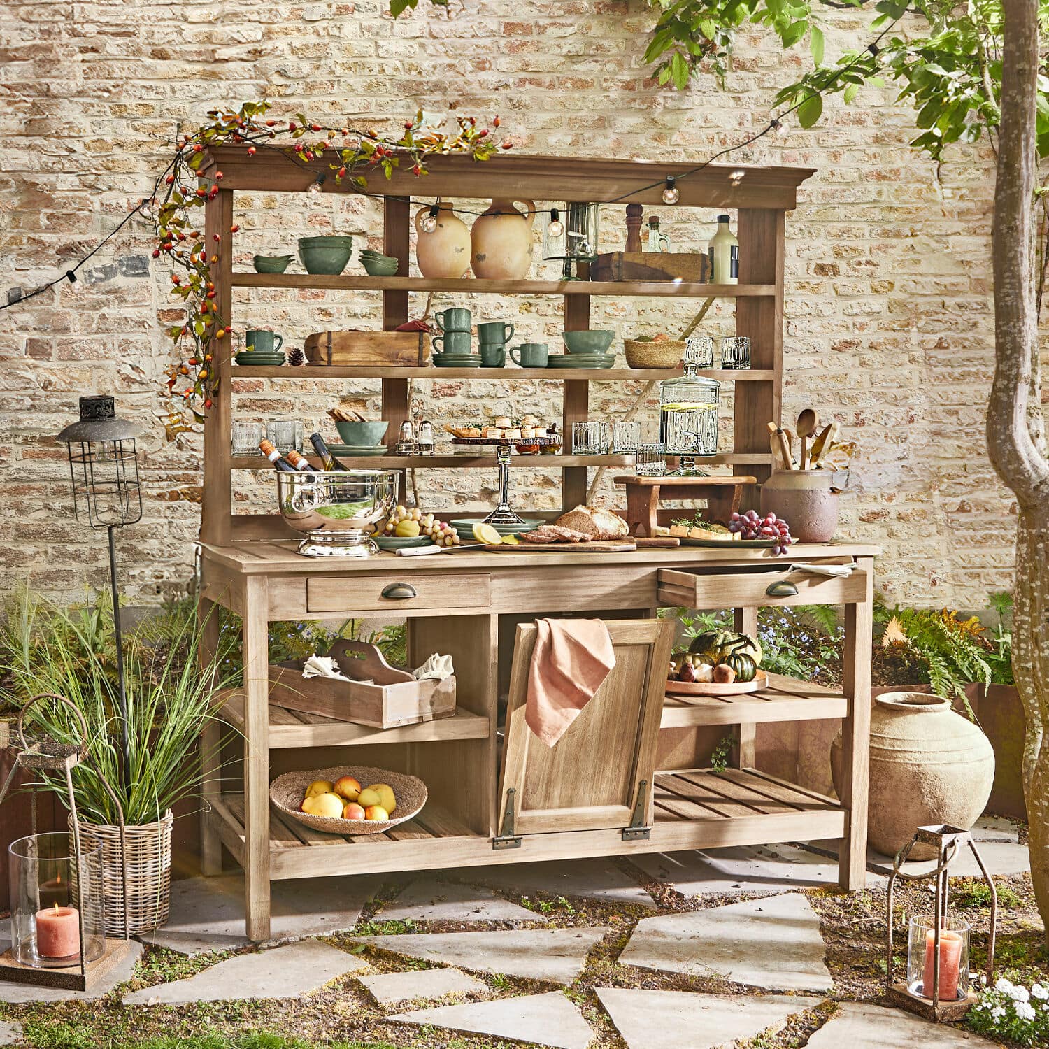 Buffet de jardinage Fallon Meuble de jardin en bois avec étagères et tiroirs, décoré de vaisselle et nourriture sur patio