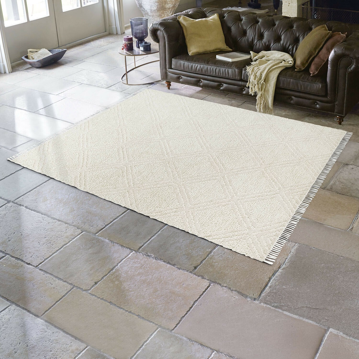 Tapis d'intérieur et d'extérieur Bruand Tapis beige à motif géométrique sur sol en pierre dans un salon avec canapé en cuir marron