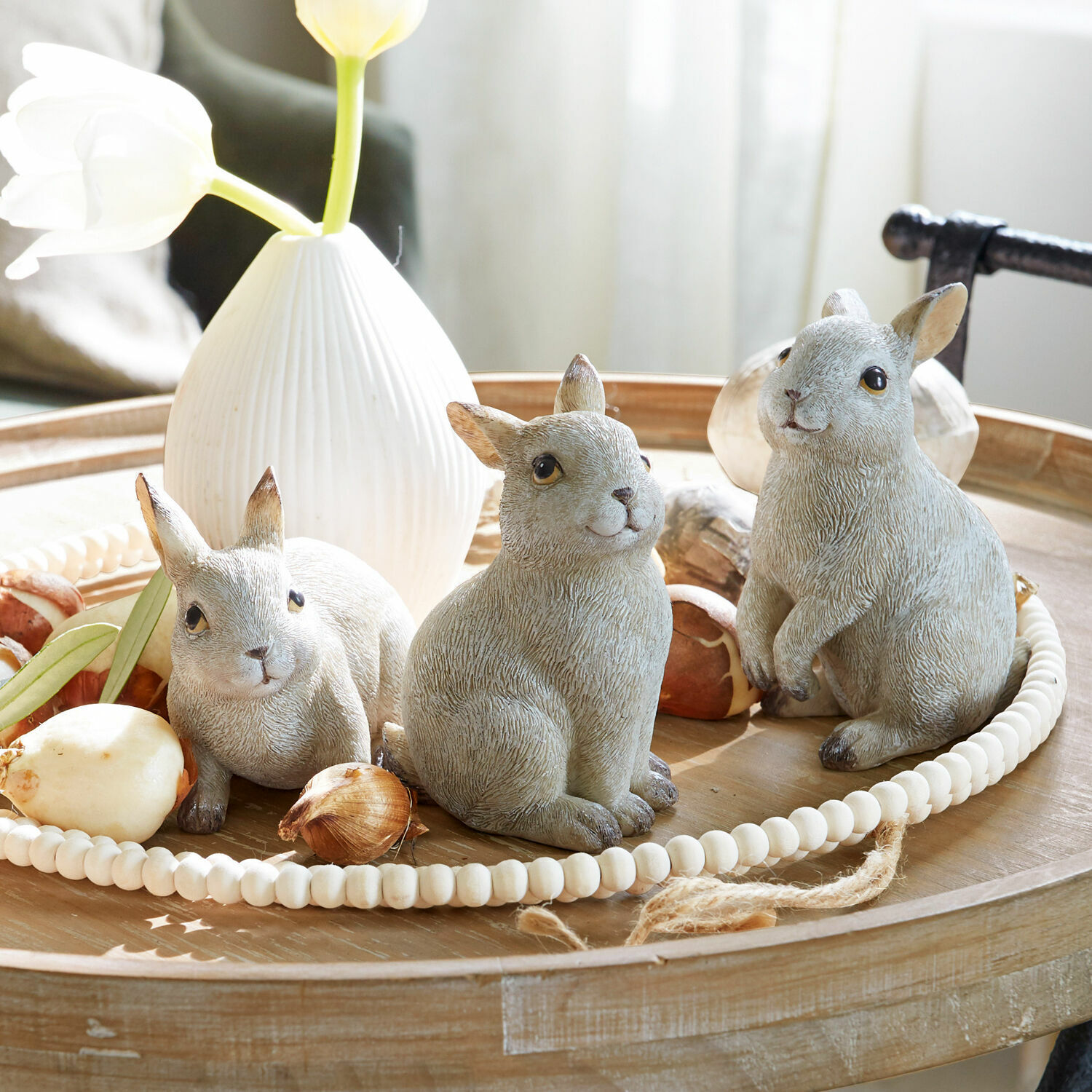 Lot de 3 lapins Anthony Trois figurines de lapins gris sur un plateau en bois avec un vase blanc et des bulbes de fleurs