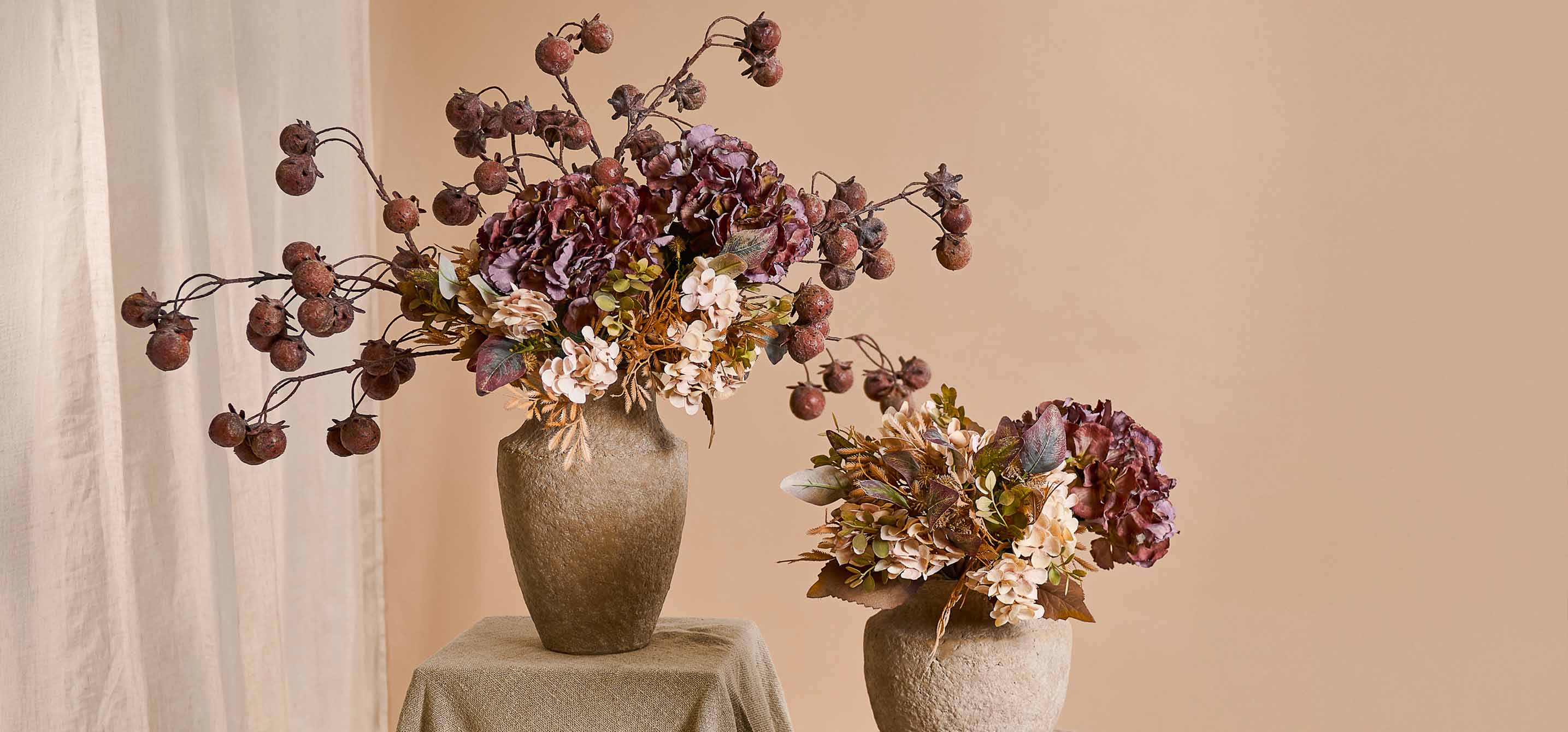 Deux vases décoratifs en pierre beige avec bouquets de fleurs artificielles et fruits aux tons chauds
