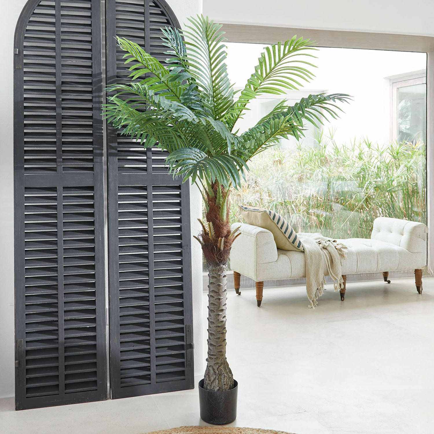Plante décorative en pot Zephyriel Palmier artificiel en pot noir dans un salon lumineux avec canapé beige et grande fenêtre
