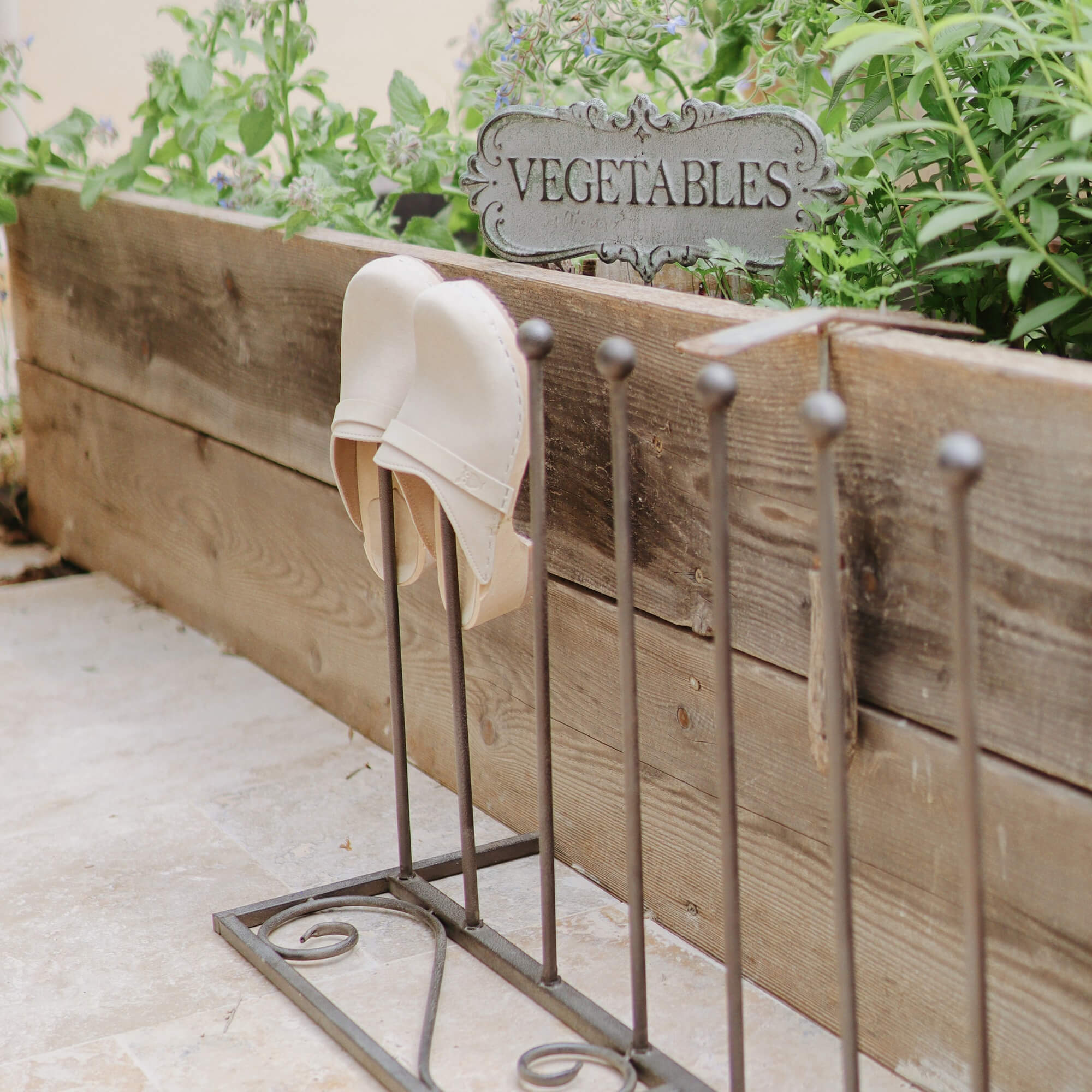 Porte-chaussures en métal avec mules blanches en cuir devant un bac à plantes en bois