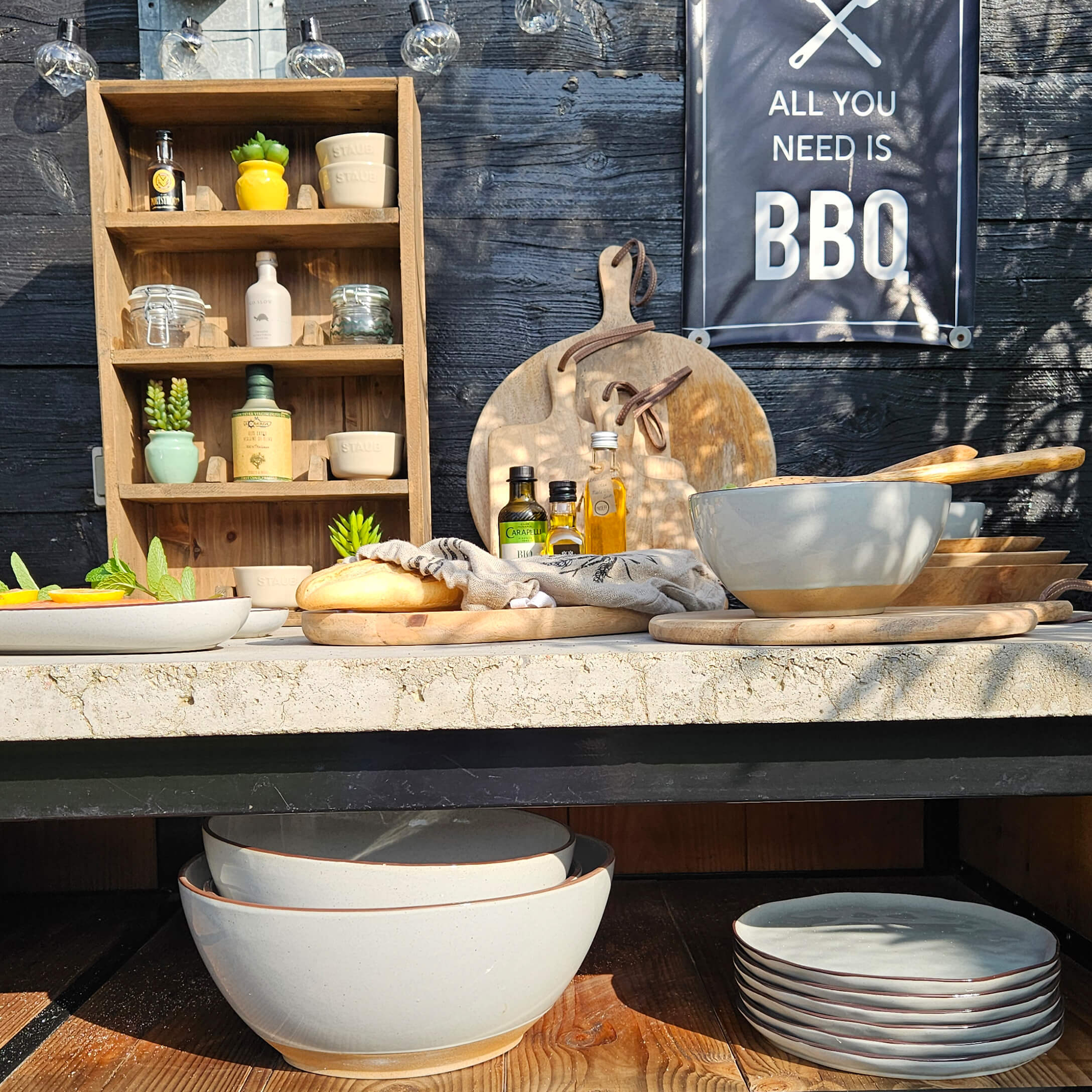 Ensemble de bols et assiettes en céramique beige avec planches à découper en bois et bouteilles d'huile sur table de barbecue