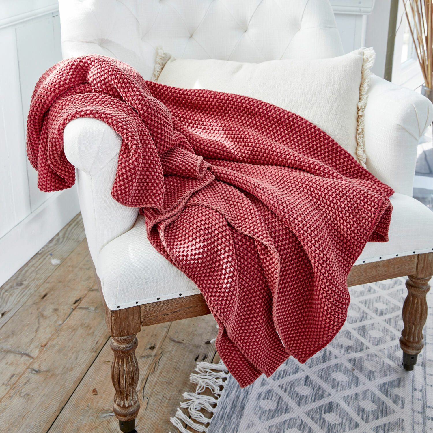 Plaid Amberley Plaid rouge tricoté en tissu doux sur un fauteuil blanc dans un intérieur lumineux