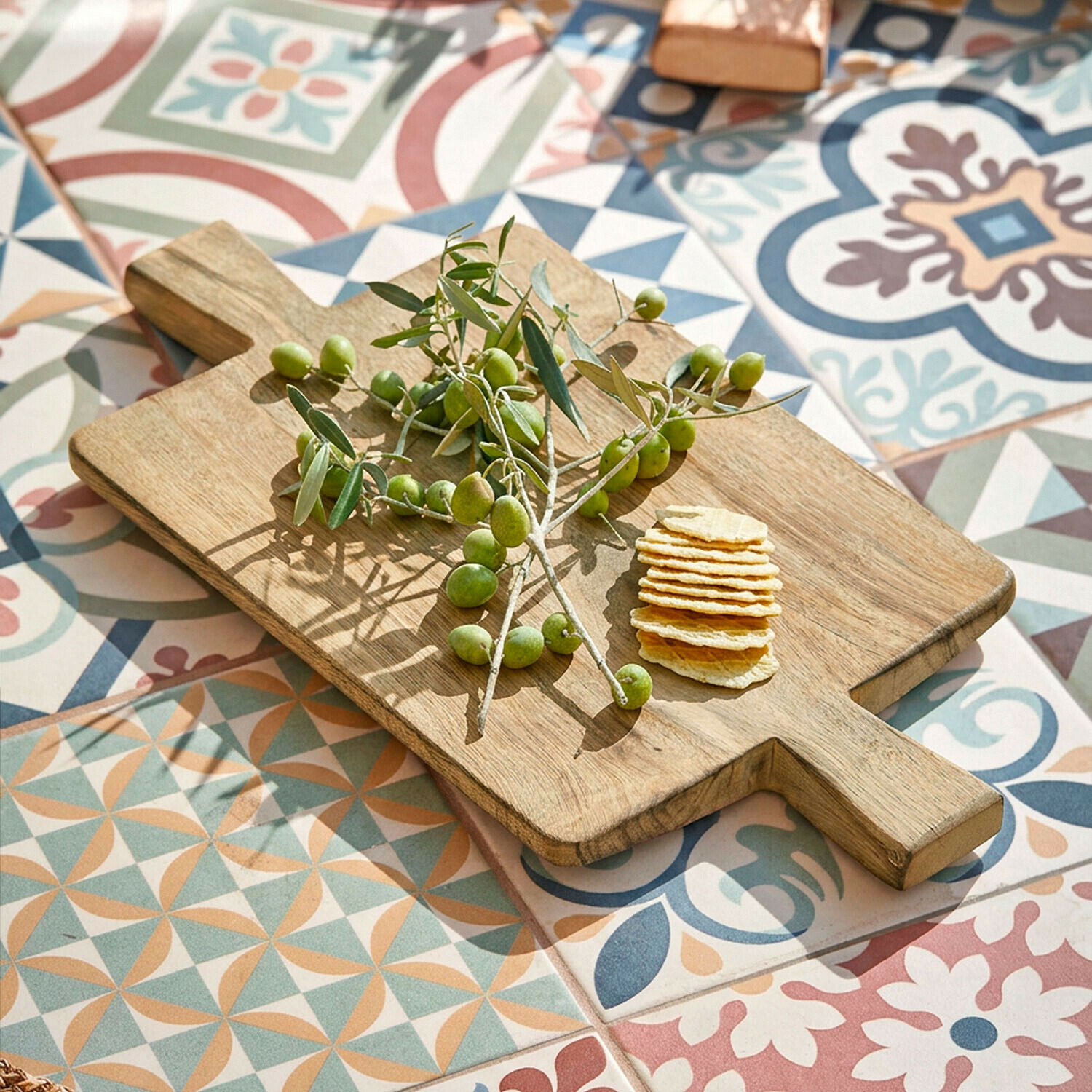 Plateau Vinoros Planche à découper en bois avec olives vertes et crackers sur un sol en mosaïque colorée